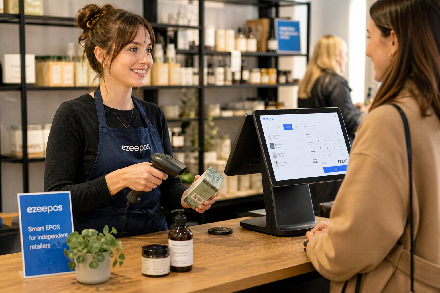 Barcode Scanning for Faster Retail Checkouts, photorealistic commercial photography of a modern UK independent shop counter during a busy day, with a staff member using a handheld barcode scanner beside a clean touchscreen EPOS terminal while serving a customer, products visible on the counter and organised shelves in the softly blurred background, realistic retail setting, warm natural lighting, shallow depth of field, subtle blue brand accents on the till interface and small signage, premium but authentic composition, technology clearly in focus, friendly service atmosphere, clean uncluttered checkout area, suitable as a WordPress featured image for ezeepos.