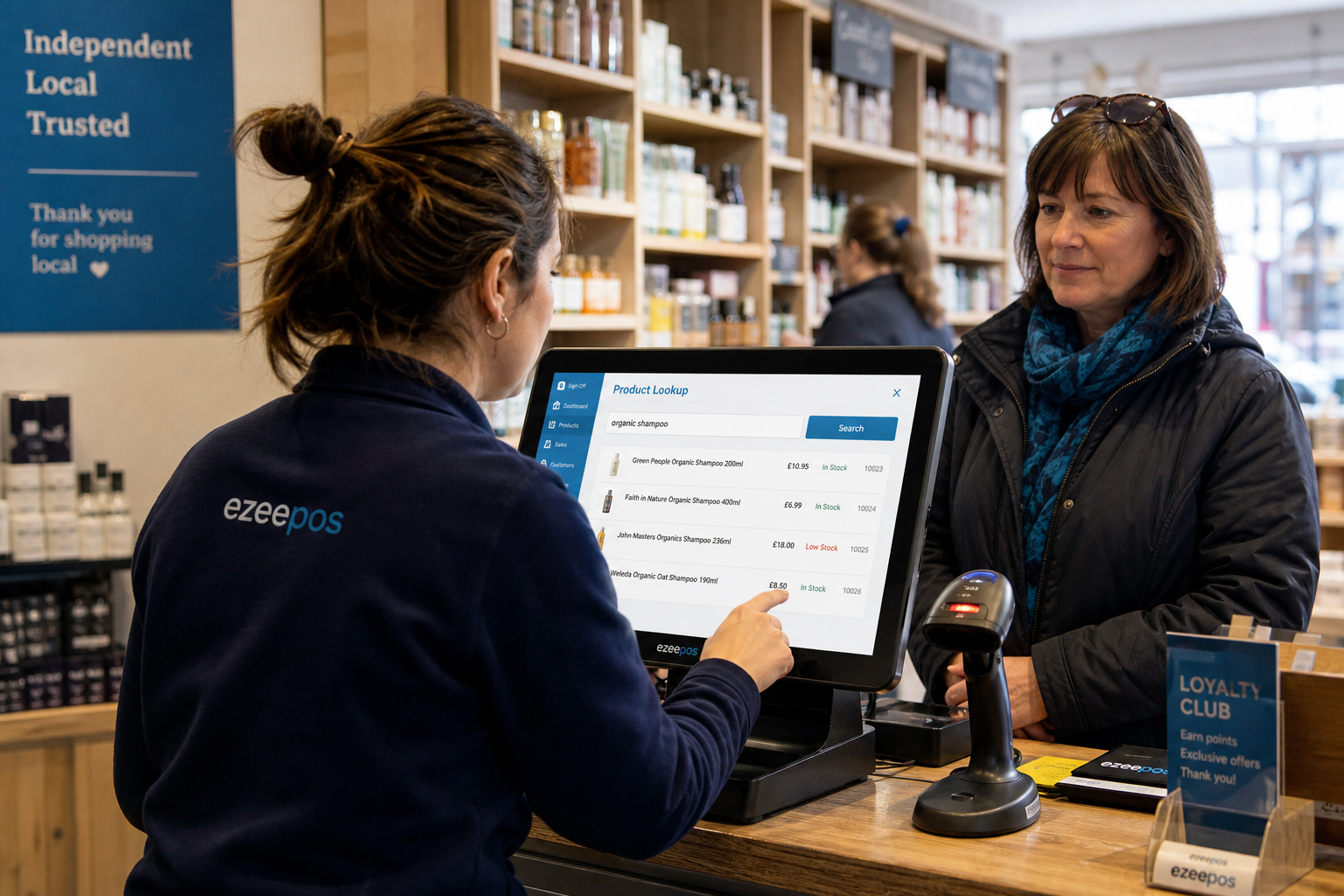 How Product Lookup Helps Busy Retail Checkouts Stay Moving, a photorealistic commercial photography style image of a busy independent UK retail shop counter with a modern touchscreen EPOS till showing a product lookup screen, a barcode scanner nearby, a member of staff quickly searching for an item while serving a customer, shelves of mixed retail products in soft focus behind them, warm natural lighting, clean counter area, subtle blue brand accents on the screen interface and shop signage, realistic professional composition with shallow depth of field, premium but authentic local shop environment, technology clearly central to the scene, suitable as a WordPress featured image for an ezeepos blog post about speeding up retail checkouts and reducing delays when items need to be found at the till.